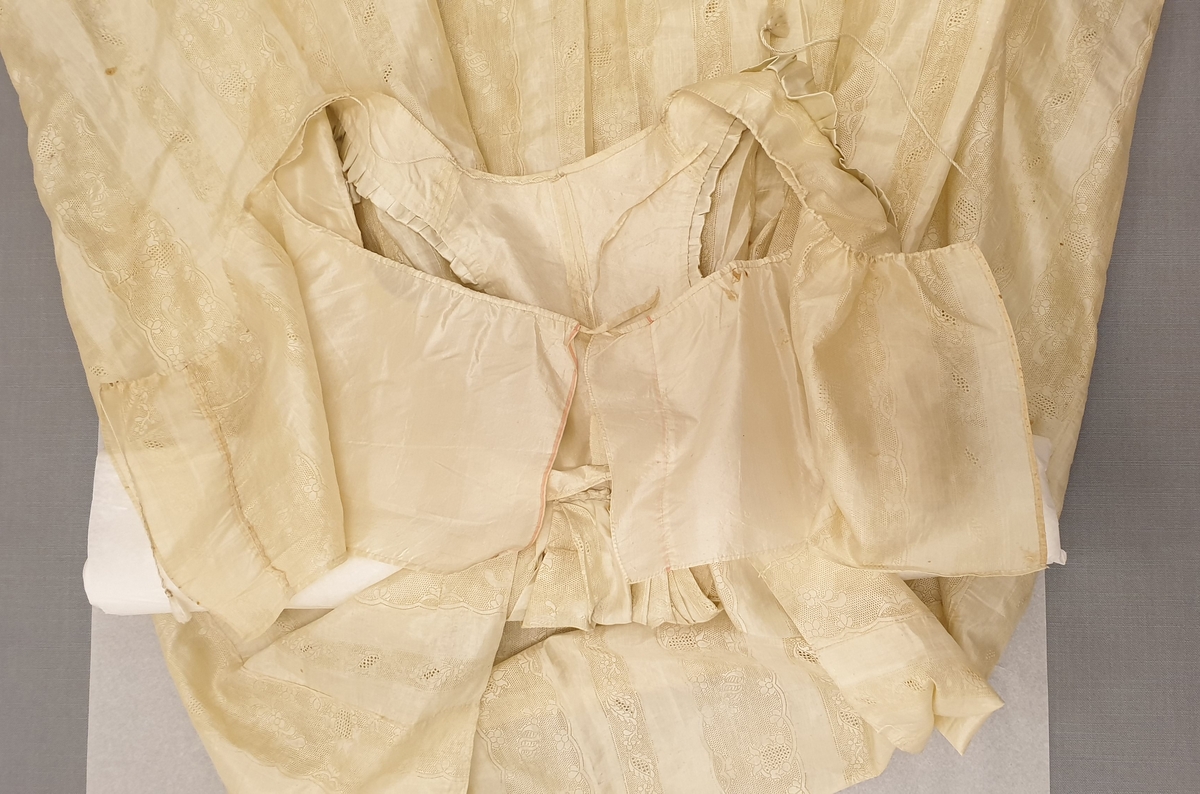 Brudklänning i empirstil från Torpa stenhus, 1815. Naturgul sidenjapon med stansat spetsmönster i form av bredare och smalare bårder med hål- och blommönster. Ärmlöst, kort liv; ärmhålen kantade med rynkad sidensatin. Djup urringning med dragsko av tvinnat silke med tofs i var ände, framstyckena utan knäppning. Innerfoder med dragsko av platt sidenband i ringningen, förövrigt ingen knäppning. Smalt ryggparti, livet endast fastsytt i kjolen mitt bak.

Kjolen samlad i flera veck mitt bak, i övrigt rak med långt släp. Nederkanten kantad runt om med ca 7 cm brett stycke sidensatin med fastsydda veckade rosetter i flortyg.