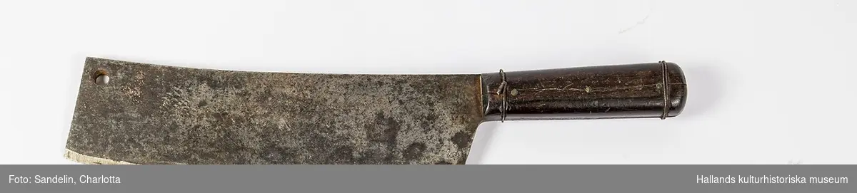 Köttyxa med långt brett blad (trubbig knivmodell) i metall och skaft av metall skott med två träsidor fäst med tre mässingsnitar (?). Träsidorna även förstärkta med två runtlöpande ståltrådsband. I huggändan på yxans oskarpa sida finns centimeterstort cirkulärt hål. Bladet svagt böjt. Märkning: Inslaget i yxbladet: "Eskilstuna Jernmanuf". "Aktiebolag", samt logotyp med Krona, ankare och ett "E".