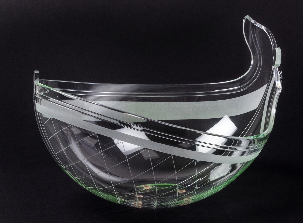 Skål av glas, formgiven av Gunnar Cyrén. Tillverkad hos Orrefors. Ofärgad. Oval form med etsat horisontalt band nära kanten. Ena änden uppdragen i fiskstjärt. Rutmönsterdekor på ena långsidan.
