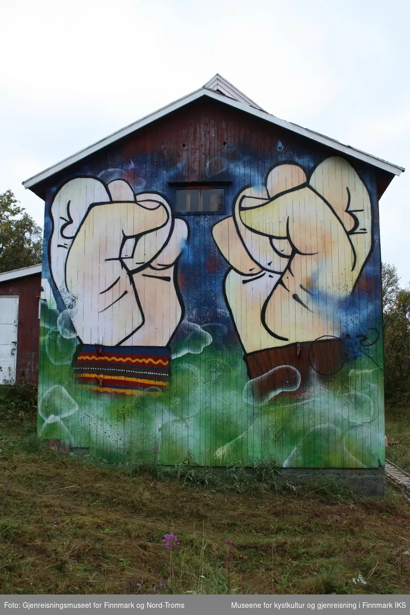 Protestleiren på Markoppneset i Finnmark i 2021. Protestbevegelsen mot dumping av gruveavfall i Repparfjorden har samlet seg og har etablert en teltleir. Bildet er del av en serie som dokumenterer leiren og omgivelsen i området.
Bildet på naustveggen er et verk av kunstneren Tegson og har tittelen "Ellos vuotna".