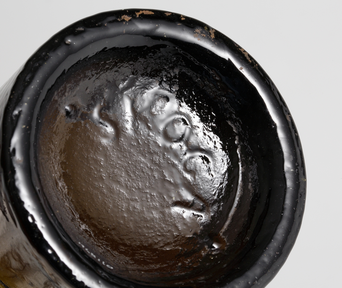 Brun flaskbotten av engelsk modell, tillverkad i tredelad järnform på Skoga glasbruk.
