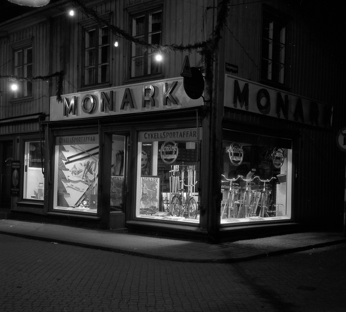 Kvällsbelysning i cykelaffär Monark i hörnet Kungsgatan-Färgaregatan, kv Friden. 1940-tal