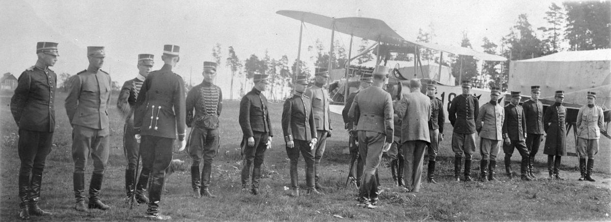 Uppställning av manskap vid krigsminister E A Nilsson besök på Flygkompaniet på Malmen den 10 oktober 1918.  I bakgrunden syns flygplan Albatros SW 12. nummer 618. I bild syns bland annat Nils Rodéhn, Ernst Fogman, Karl Amundson och Gösta D:son Carlson.