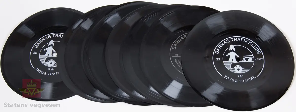 Rund utformet vinylplate (grammofonplate) for bruk på platespiller. 0,2 millimeter tykk. Sort med hvit påskrift. Det er 11 forskjellige plater, noen er det flere eksemplarer av. Beregnet for hastighet 33 RPM. Platene har spilletid rundt 5 minutter.