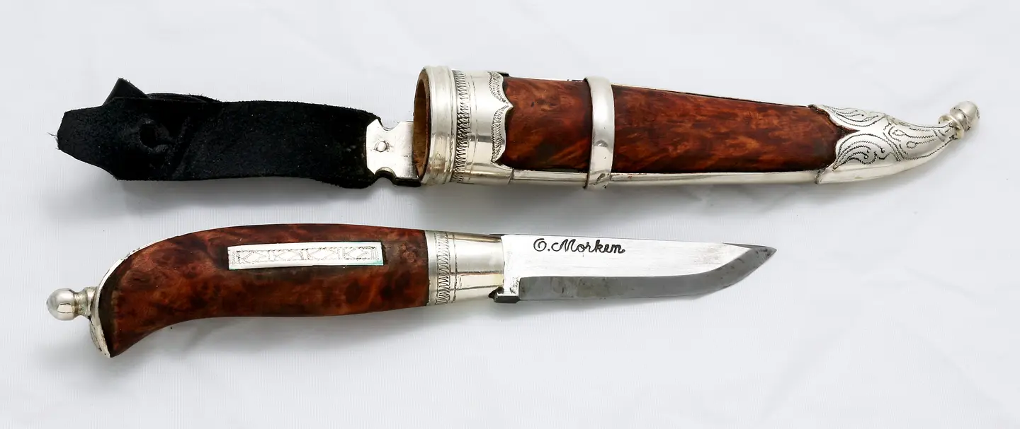 Knife by Nils Karl Magnus Karlsen with bolsters and end balls in silver. Sheath guard and handle in masur birch. Tramplings and wriggle cuts.