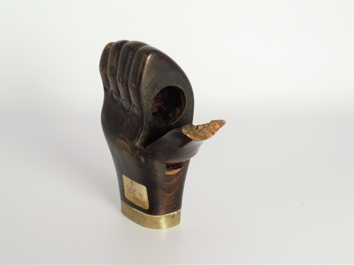 Pipehode formet som en hånd. Pipehodet har et hulrom for oppbevaring av glødende tobakk og lukkemekanisme som er formet som tommelen.