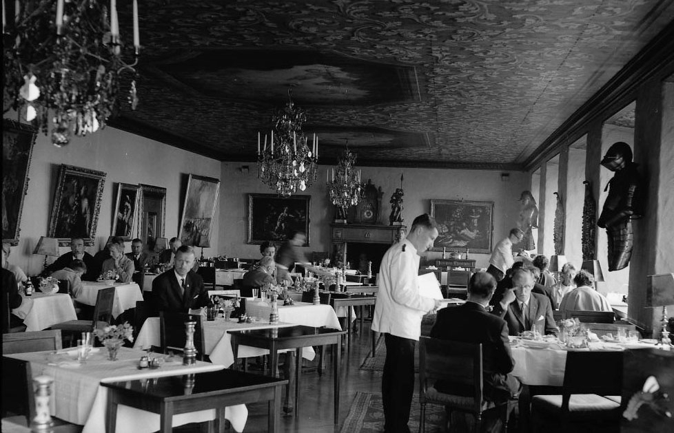 Matsalen till hotell/restaurang Gyllene Uttern med gäster. En servitör tar upp beställning.