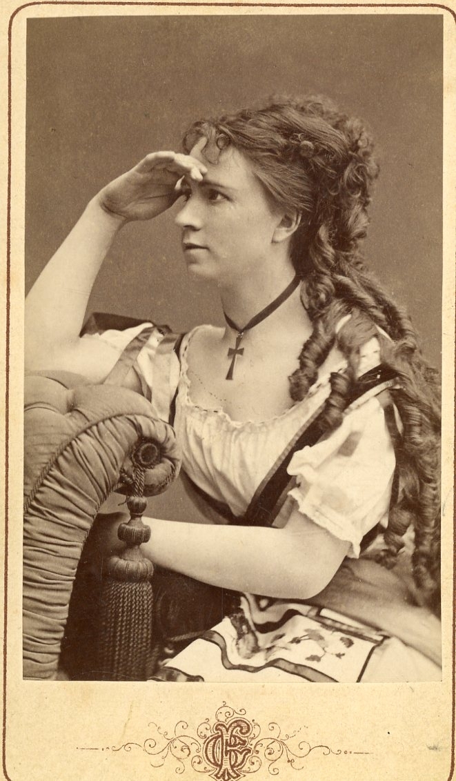 Kabinettsfotografi av en sittande kvinna som med handen ovanför ögen spanar mot vänster i bild - 3/4-profil.