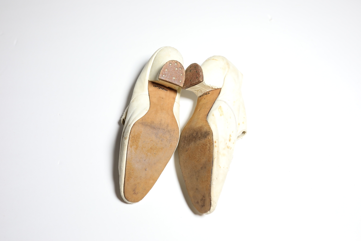 Smal sko med snellehel, er åpen til litt foran remmene. Tre remmer over som kan festet til kule på motsatt side. Perledekor foran på skoene.