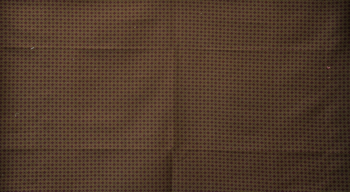 Bomullstyg, början av 1960-talet. 
Skjorttyg på 90 cm bredd. Tryckt mönster med små vinröda figurer med svarta prickar på styckfärgad olivgrön botten.
Rapport 1,8 x 1,8 cm.
Tryckfärger 2.