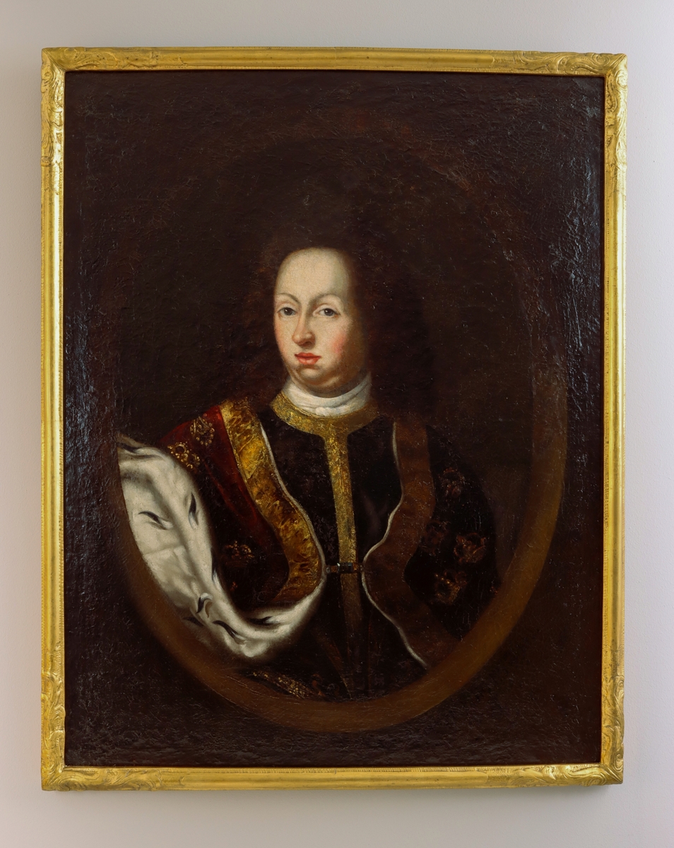 Porträtt föreställande Karl XI. Bröstbild. Karl XI med mörkt hår, klädd i mörk dräkt med vit krage och bräm i guld. Över dräkten en röd mantel med kant och detaljer i guld, samt fodrad med hermelin. Mörk bakgrund med oval ram.