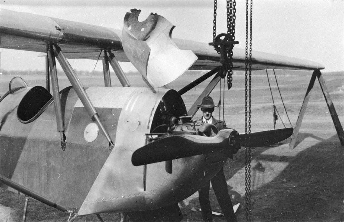 Närbild av nos på civilt flygplan Petterson S-81 (Planet Pettson) under slutmontering, 1924. På plats vid F-hangarerna på Malmen. En man står vid bredvid. Planet konstruerades och byggdes av ingenjör Hugo Petterson (senare Bertler). Planet registrerades år 1932 som SE-ADD.
