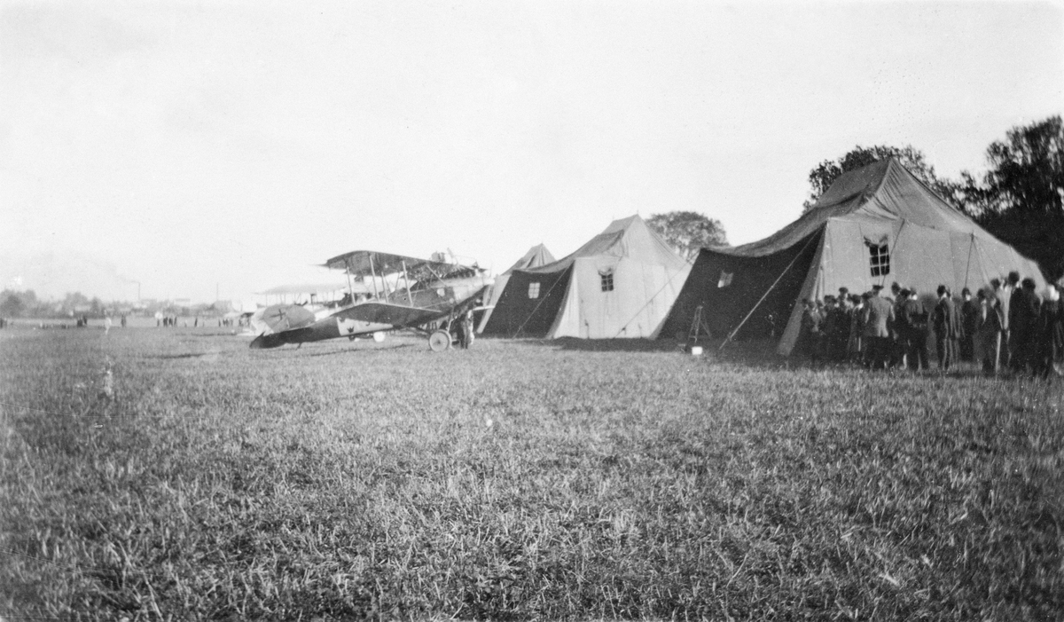 Flygplan FVM S 18 uppställt på flygfält omkring 1919-1924. Vid tälthangarer och folksamling.