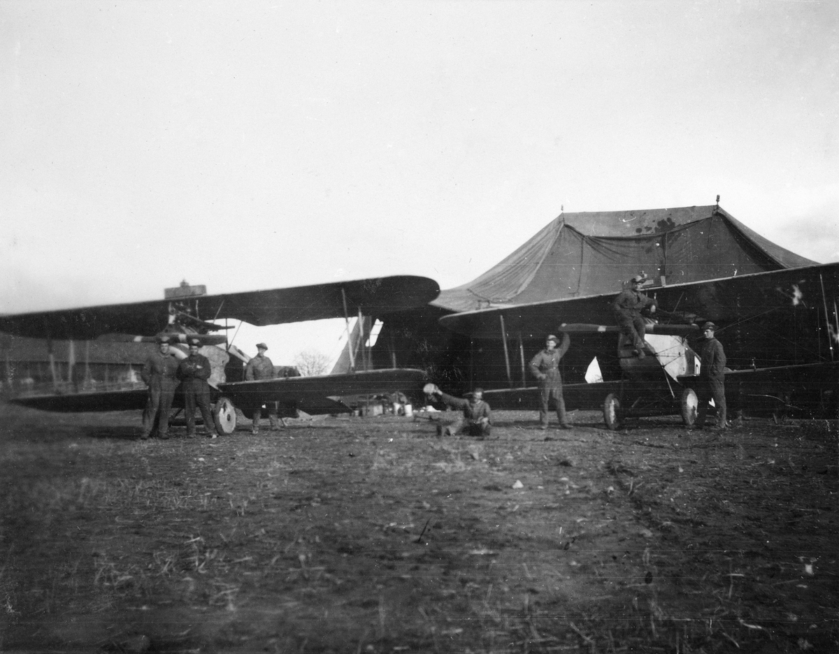 Två flygplan J 1, Phönix D. II uppställda framför tälthangarer, omkring 1920-1926. Sju militärer vid flygplanen.