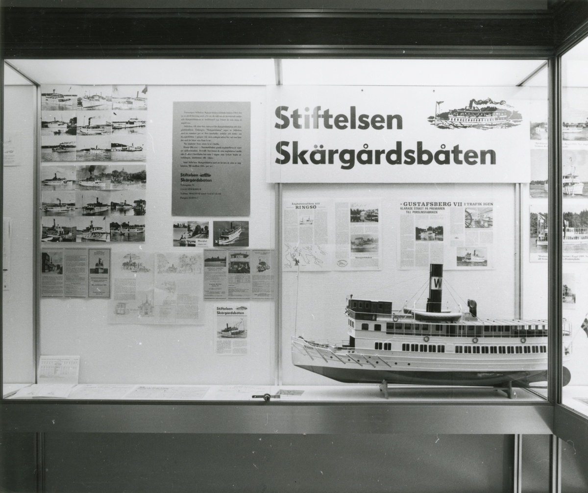 Utställningen Skärgårdsbåtarna. Trappmonter med montage av fotografier och artiklar om Föreningen Stiftelsen Skärgårdsbåten samt en fatygsmodell av SAXAREN.