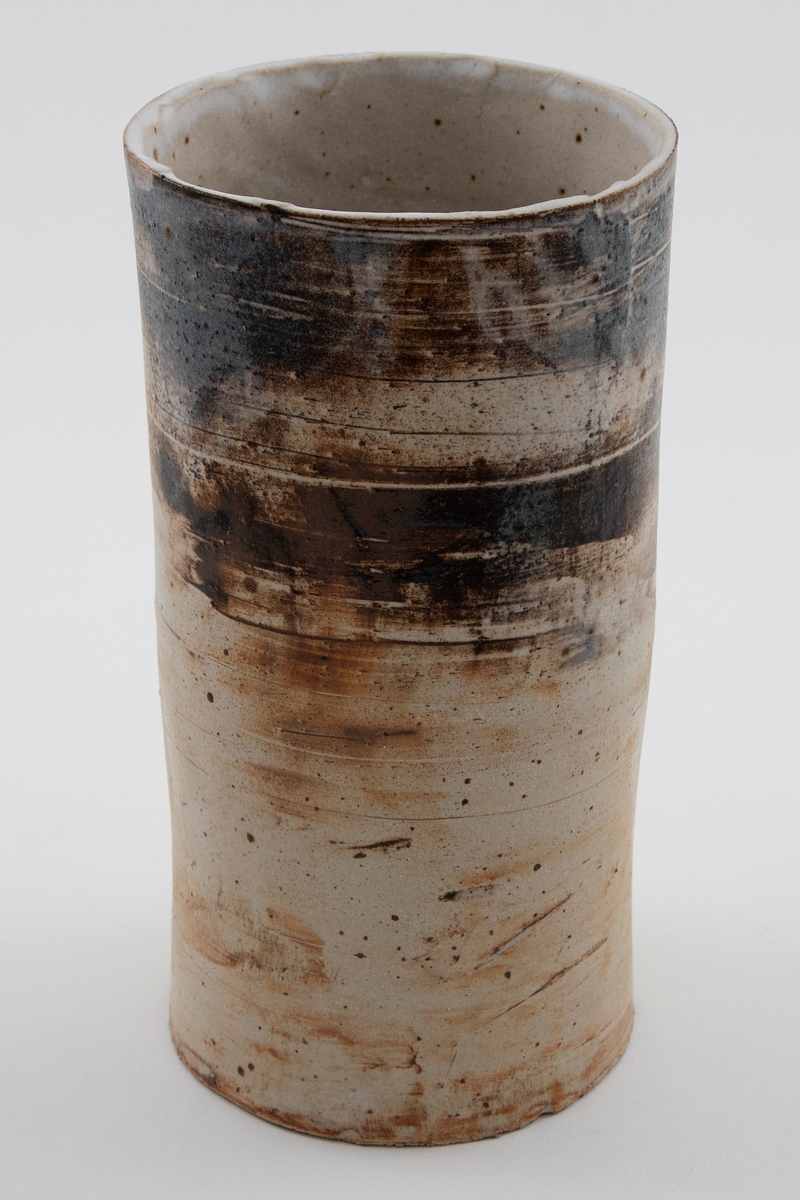 Høy sylinderformet vase i glasert steingods. Hvit med rustrødt skjær og svartspettet på øvre del av korpus.