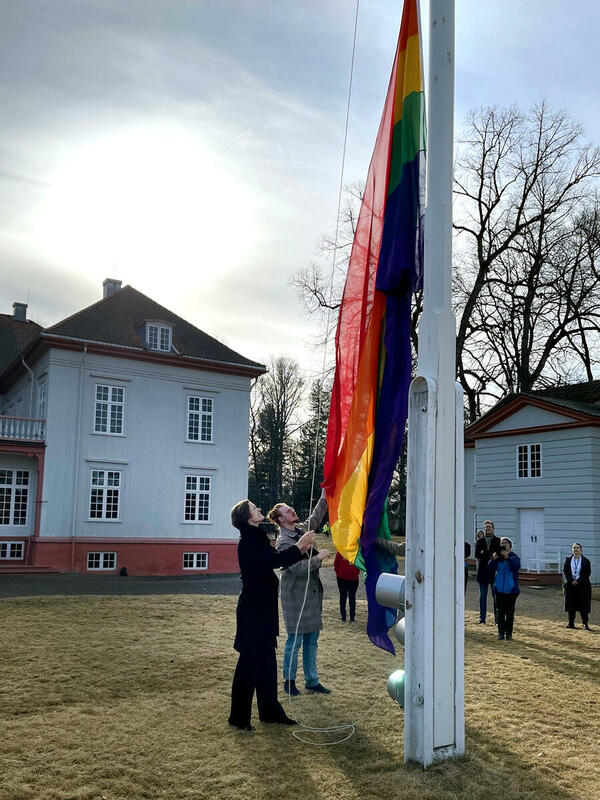 Kulturminister Annette Trettebergstuen heiser regnbueflagg i flaggstanga ved Eidsvollsbygningen
