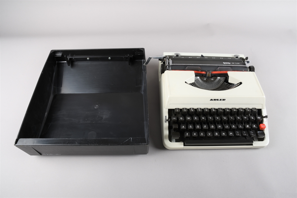 Berbar skrivemaskin/reiseskrivemaskin med koffert/deksel som klipsast på skrivemaskina når denne ikkje er i bruk. Kofferten har handtak i framkant. Skrivemaskina har querty-tastatur og fargeband i raudt og svart.