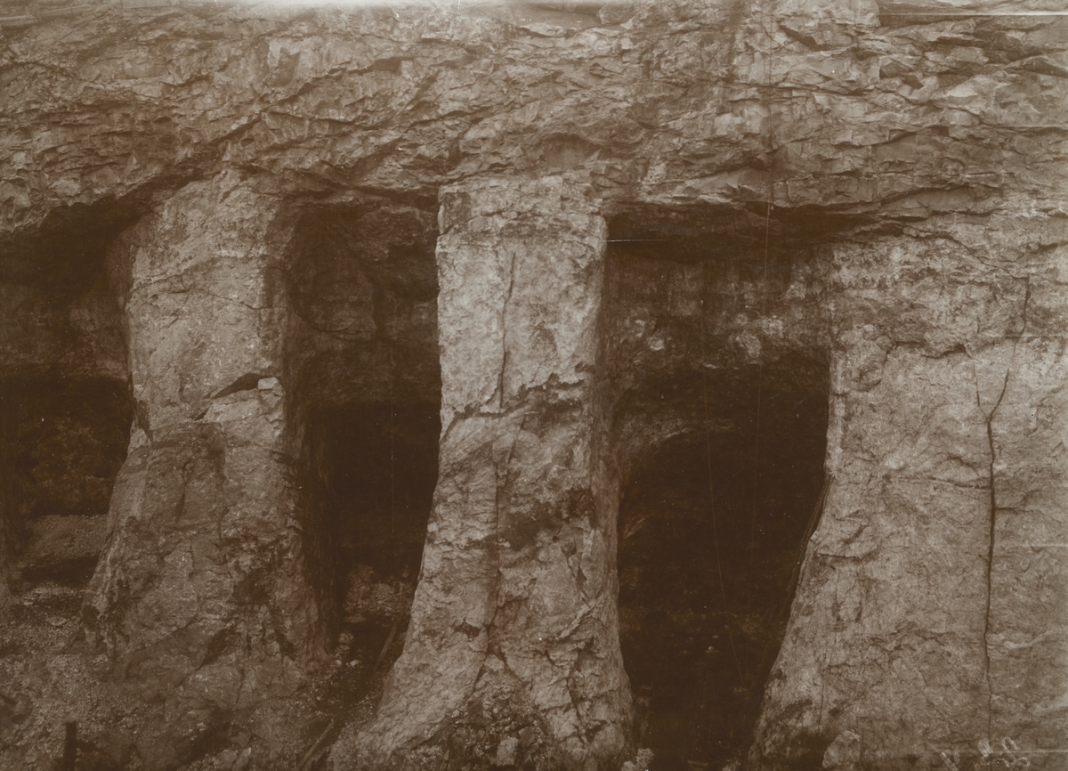 Fotografi från expedition till Grönland. Motiv av stenpelare uthackade i berg med grottor bakom.
