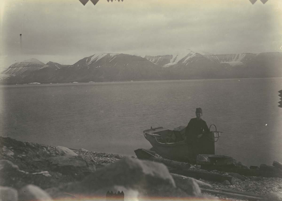 Fotografi från expedition till Spetsbergen 1920. Motiv av man med liten träbåt på strand vid vatten.