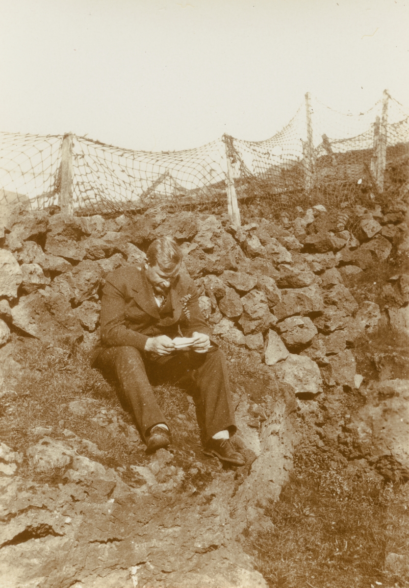 Fotografi från Albin Ahrenbergs resa till Grönland 1929. Motiv av man som sitter och läser på stor sten.