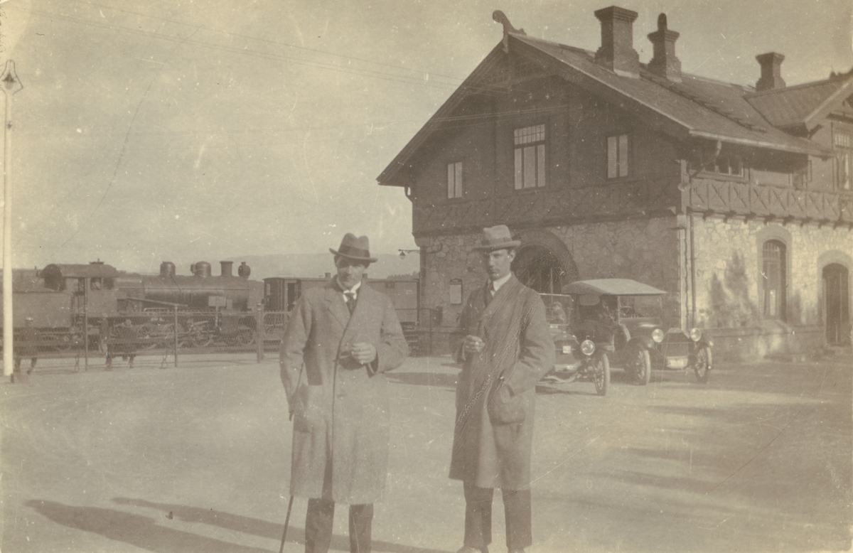 Fotografi från Albin Ahrenbergs resa till Grönland 1929. Motiv av två män som står framför hus, bilar och tåg.