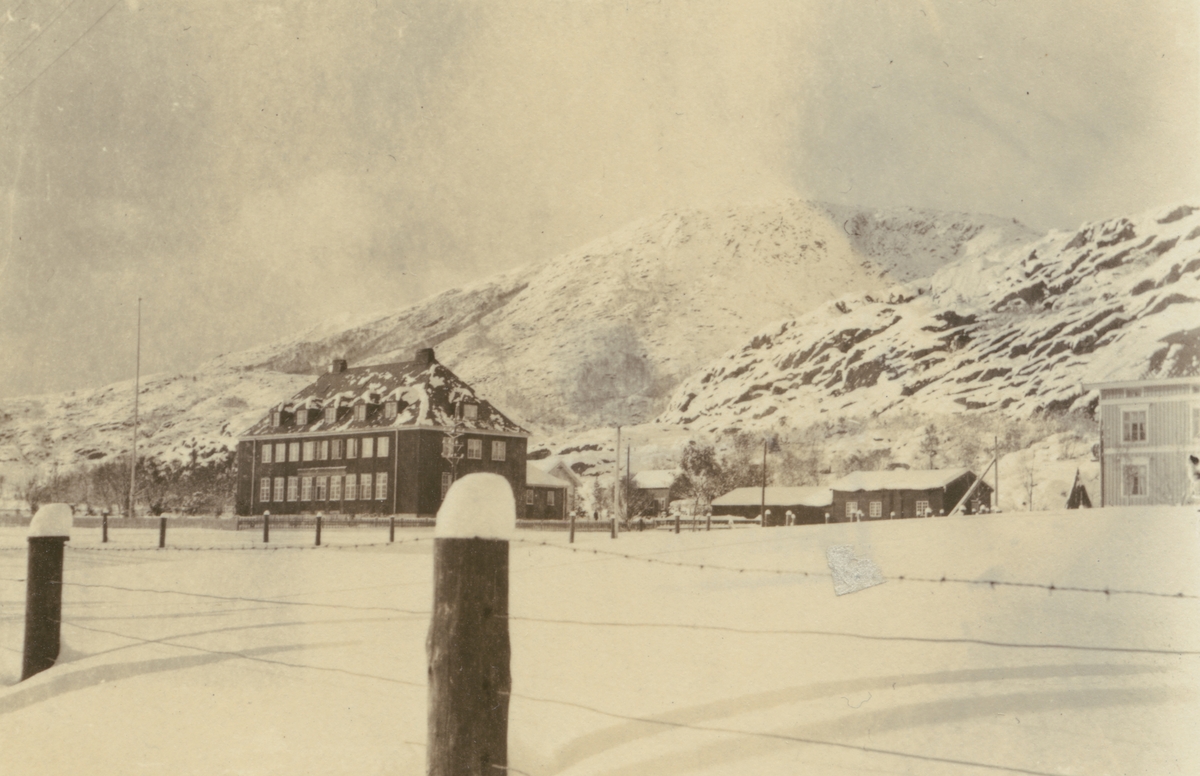 Fotografi från Albin Ahrenbergs resa till Grönland 1929. Motiv av hus i snötäckt bergslandskap.