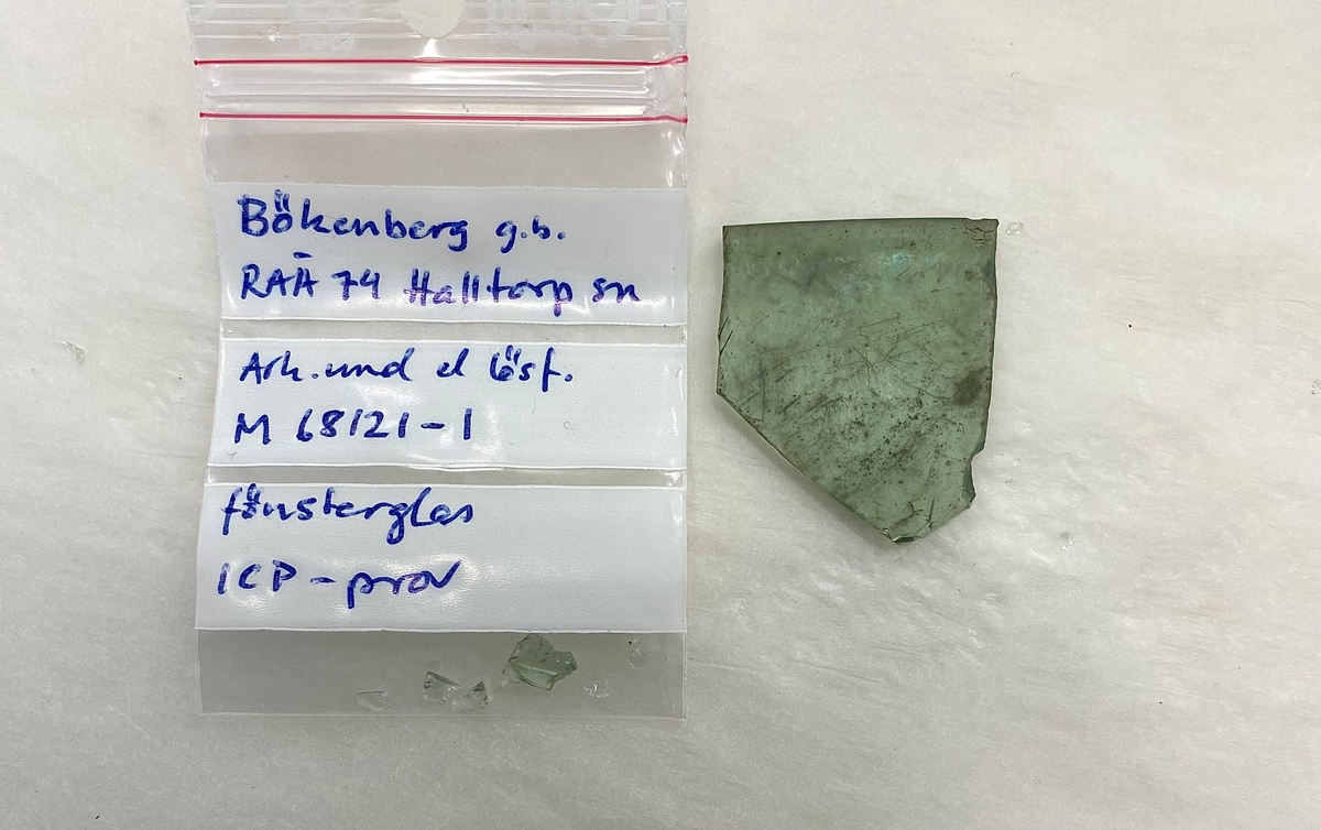 Fönsterglasfragment i grön glasmassa med en mjukt rundad sida. Fragmentet lämnat för ICP-analys i januari 2023. Se bild 2.