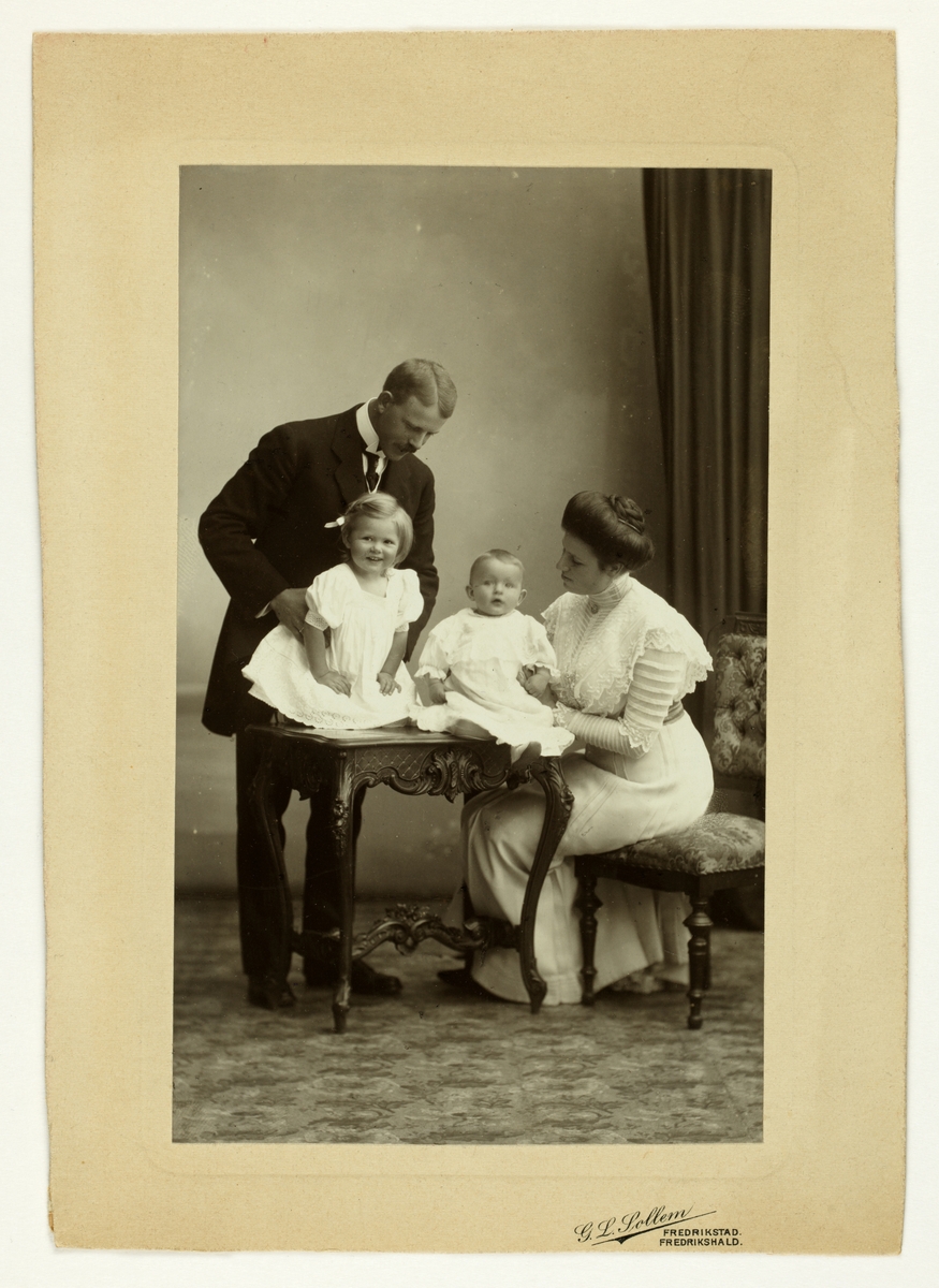 Familiebilde, to barn sitter på et bord mens to voksne mennesker støtter de. Westye Parr Egeberg og hans kone Nini (f. Wedel Jarlsberg) med sine døtre Mimi (Hanson) og Lucy (Høegh).