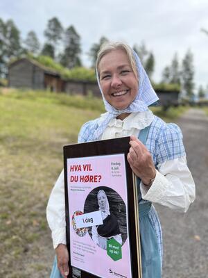 Dame i blå kjole som holder en plakat og ler