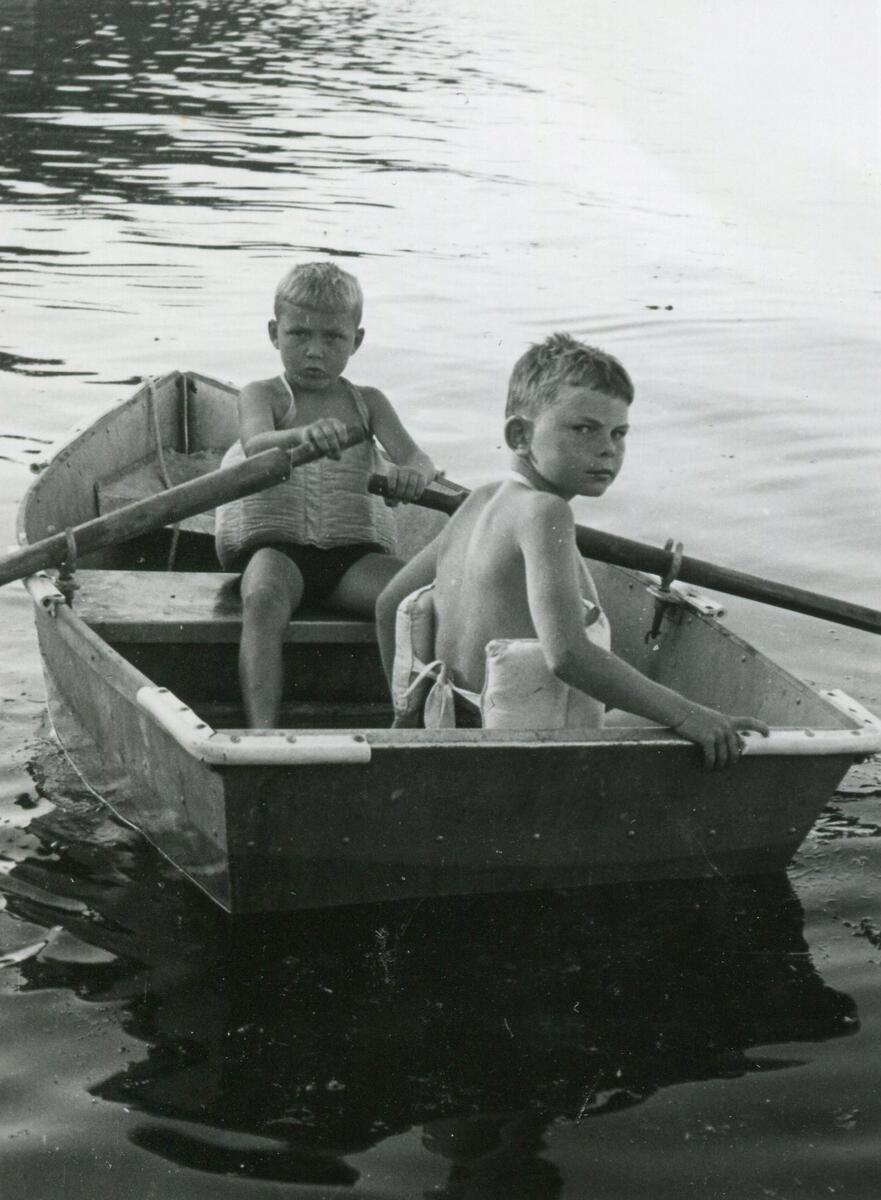 Svart/hvitt bilde av to gutter med svømmebelte i en jolle
