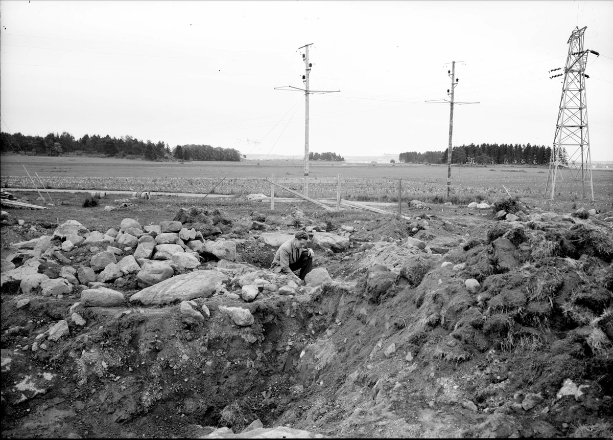 Man sittande på huk på området med de avtorvade gravarna, Brillinge, Vaksala socken.