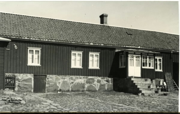 Boningshus på stenfot med veranda tillhörigt Liden 12:2 i Backa, Värö. Till höger om verandan står mjölkkannor och till vänster finns en källardörr i grunden.