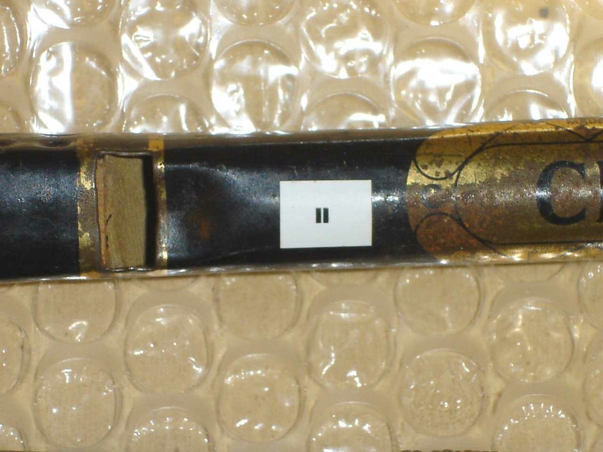Blikkfløyte laget av plate som er bøyet til et omvendt konisk rør. Blokk av tre. Malt svart med en enkel gull-dekor.
Identisk med RMT 87/48 "Tin whistle"
Seks fingerhull.