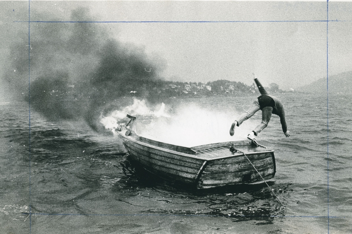En person er i ferd med å hoppe fra en brennende båt.