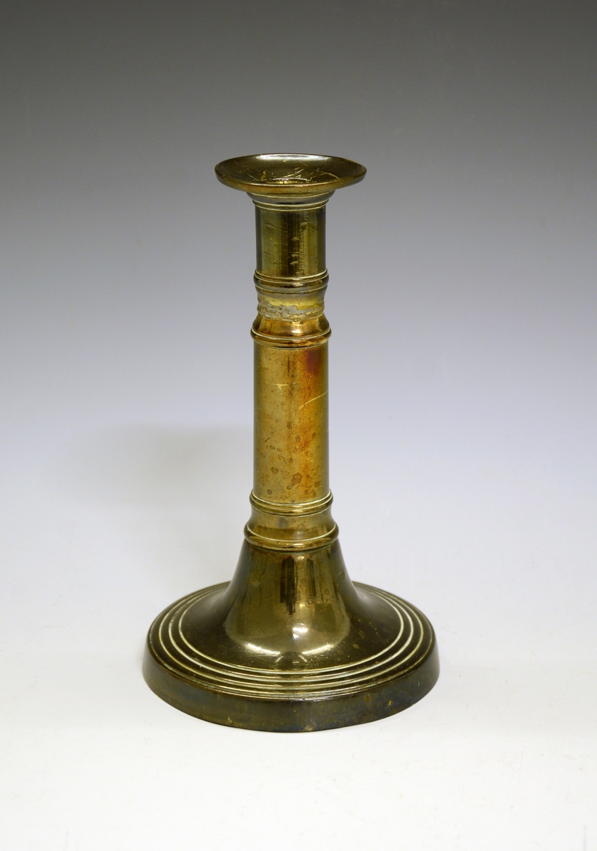 Lysestake av legeringsmetall, "heilrend", med sylinderformet pipe med et par innsnøringer og sirkelformet hov (fot). Pipen er loddet.