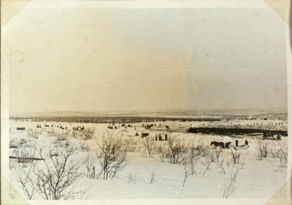 Bildet viser mange mennesker som bygger en flyplass i nærheten av Kautokeino. De bruker hester og sleder som hjelpemiddel. Det karrige landskapet er dekket med snø. Bildeforklaringen nevner besøket av Bernt Balchen, antagelig med et fly at type Dakota.