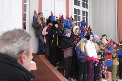 En gruppe elever står i trappa til Eidsvollsbygningen, vendt mot gårdsplassen og synger. De har samiske håndflagg.
