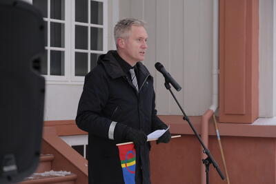 Direktør ved Eidsvoll 1814, Bård Frydenlund, ståår foran Eidsvollsbygningen i vinterklær og snakker i mikrofon. Han har et samisk håndflagg i hånden