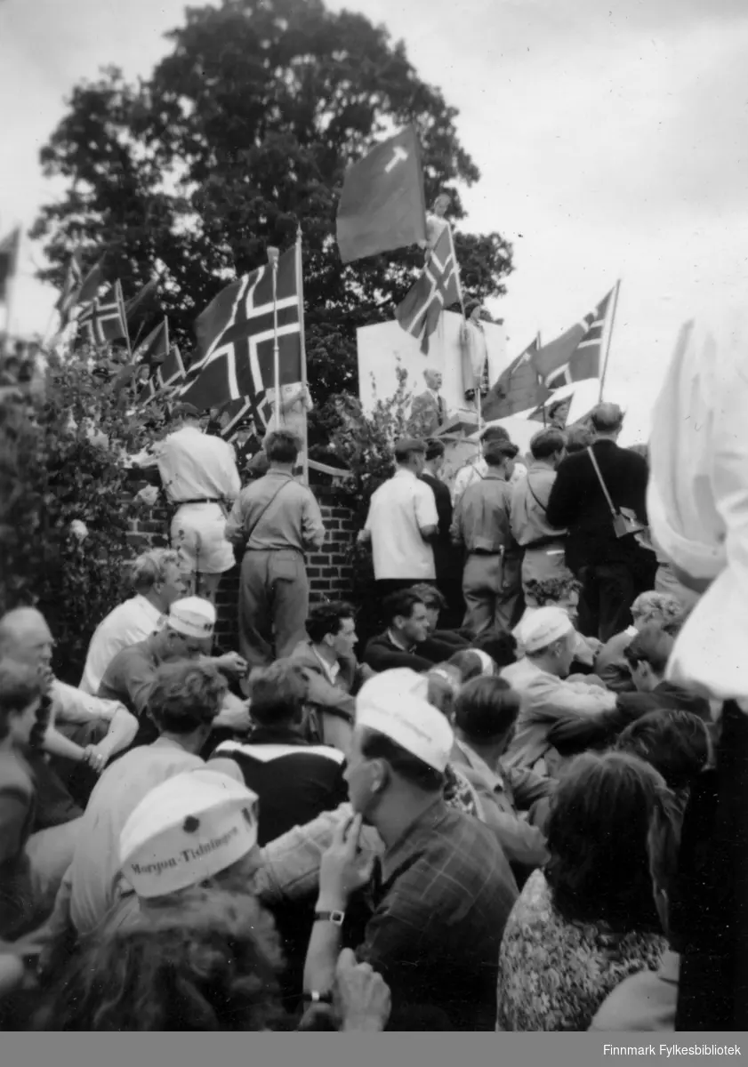 På AUF stevnet i Stockholm, 1950. Det er mange mennesker som sitter i forkant av bildet. I bakgrunnen står det flere med ryggen til. De holder flagg, blant andre flere norske-, og to russiske flagg