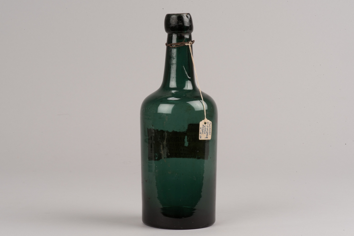 Cylindrisk mineralvattenflaska av grönt glas.
Mynningen är försluten med en nedtryckt kork.
Etiketten på flaskan är något skadad, men det framgår att buteljen är från Linköping.