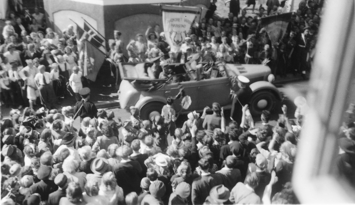 Folkemengde rundt kong Haakon, som kjøres i bil.