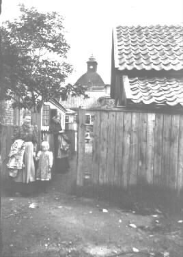 Fotot taget från väster på fortsättningen av Gröna gatan " in på gården. ´Holsterskan´ framför henne Augusta Bissmark med Gertrud, dottern". (C.E.)