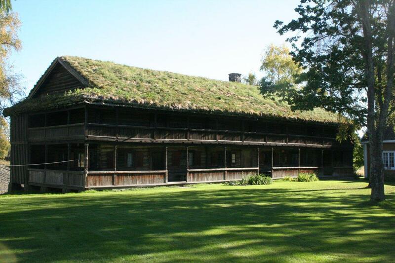 Bildet viser et stort laftet hus med en svalgang. På taket er det torv. Bildet er tatt om sommeren.