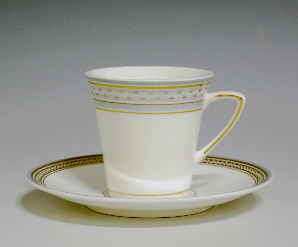 Kaffekopp av porselen med hvit glasur. Dekorert med bord øverst i blågrått og gull. Gullstrek over nedre kant og på hanken.