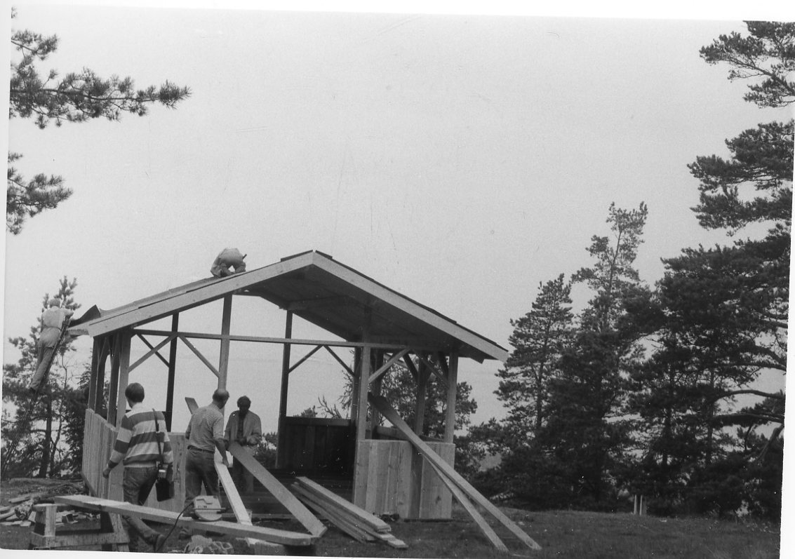 Byggnadsarbete på en paviljong på Grännaberget. En man står på en stege till vänster, en man på taket och två män arbetar med virke.