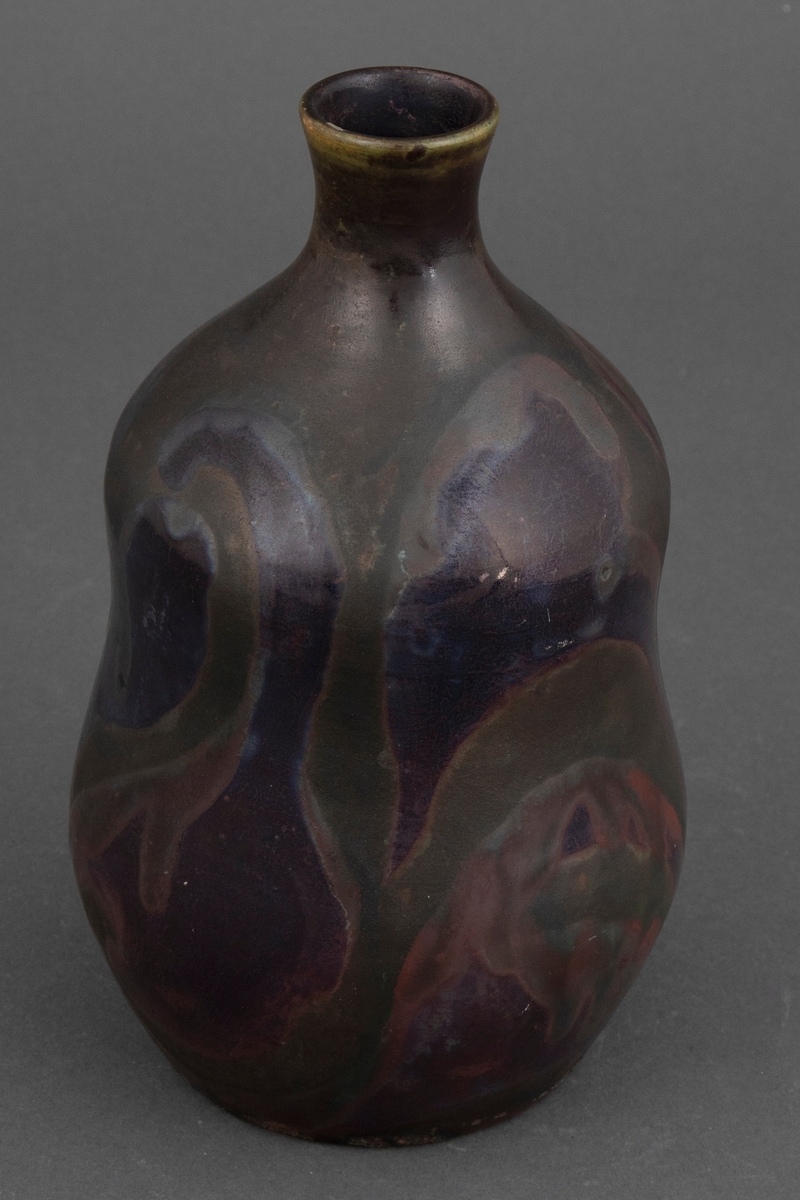 Vase med matt lusterglasur. Glalsuren er i grønnlige toner, men noen partier i rødlige og fiolette toner, og noen i matt og svakt lustret grønn.