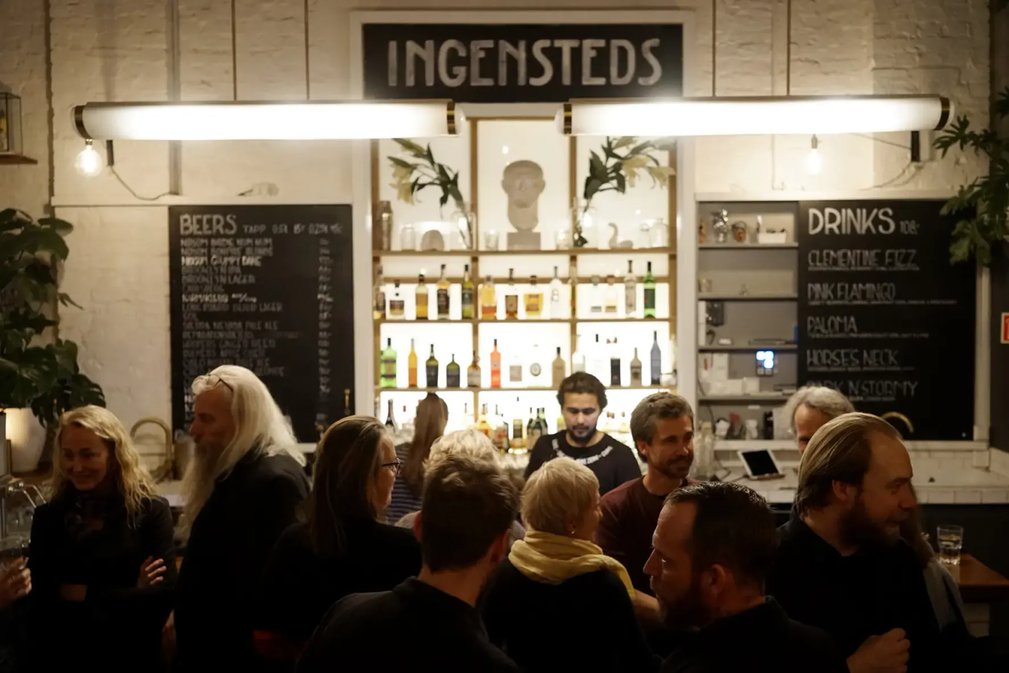 Mange mennesker på en bar, skiltet "Ingensteds" kan leses høyt oppe på veggen.