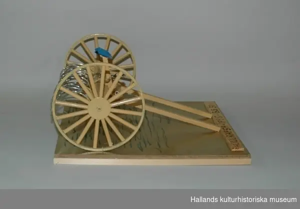Detta är en modell av en hjulräfsa där alla delar är rörliga. Den står på en träplatta som är målad i guld och streckad med grön tusch för att likna gräs. Den har en blå sadel och räfsan är i metall. Hjulräfsan är målad gul-aprikos och sitter fast mellan två stora hjul. Två skaklar sitter på räfsan. Liten träplatta på guldplattan, där står det inbränt: HJULRÄFSA. 1925. BS. 31. Undertill på en vit lapp står det: Börje Sunesson. Nr. 31 januari 2000.