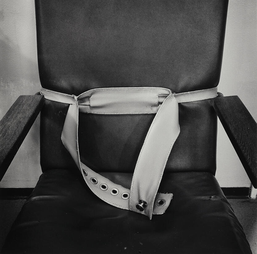 Nærbilde av en stol med belte. Fra Dag Alvengs bok Asylum fra 1986.